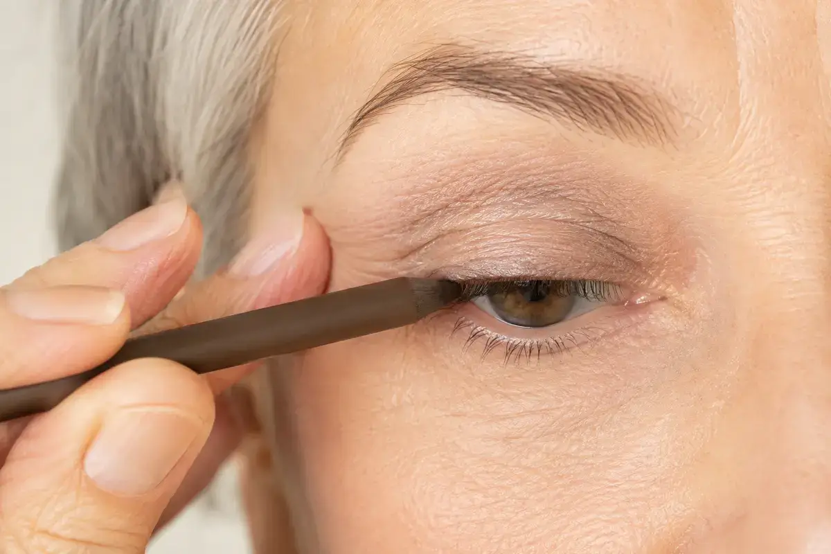 Mature woman pressing espresso eyeliner between the roots of sparse upper lashes