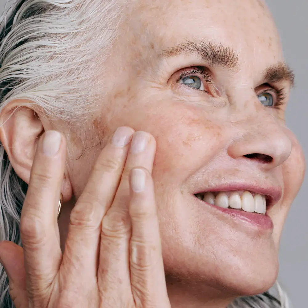 Senior woman touching her smooth cheek while admiring healthy radiant skin.