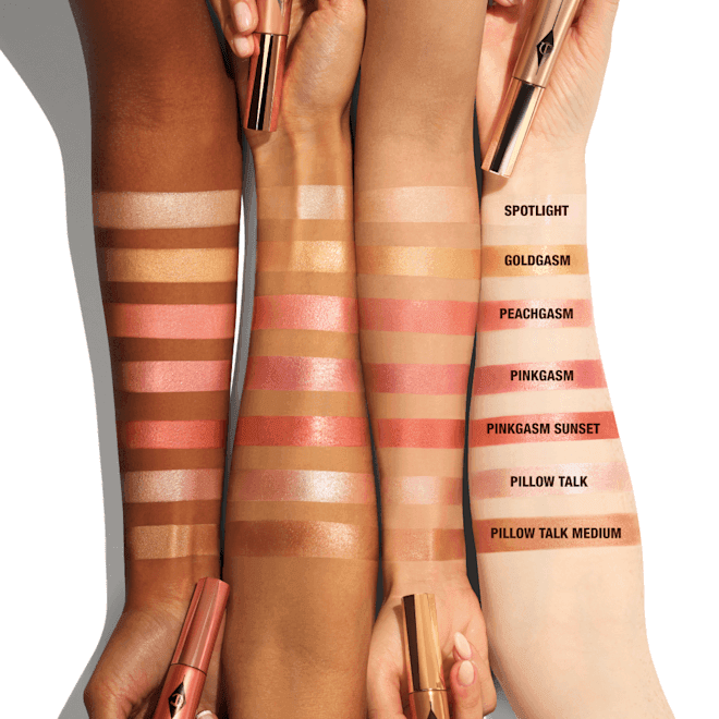 Three forearms of different skin tones display swatches of highlighter and blush shades named: Spotlight, Goldgasm, Peachgasm, Pinkgasm, Pinkgasm Sunset, Pillow Talk, and Pillow Talk Medium.