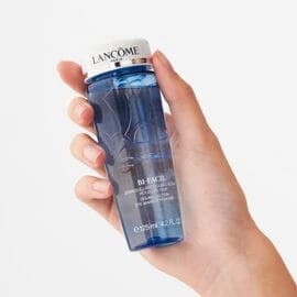 Hand holding a recognizable Lancôme Bi-Facil eye makeup remover bottle